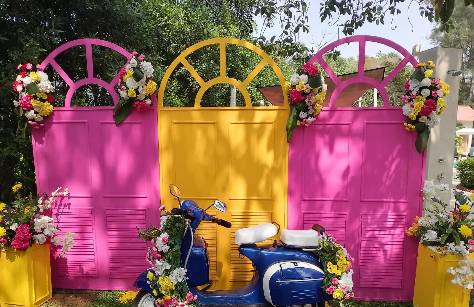 Pink and yellow vintage door photo wall with a flower-decked blue Vespa scooter prop by Imagine Decorators Goa