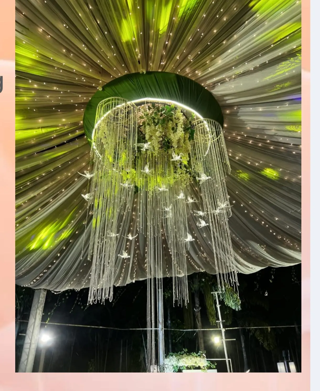 Suspended floral chandelier with hanging crystals under a draped fairy-light canopy by Imagine Decorators