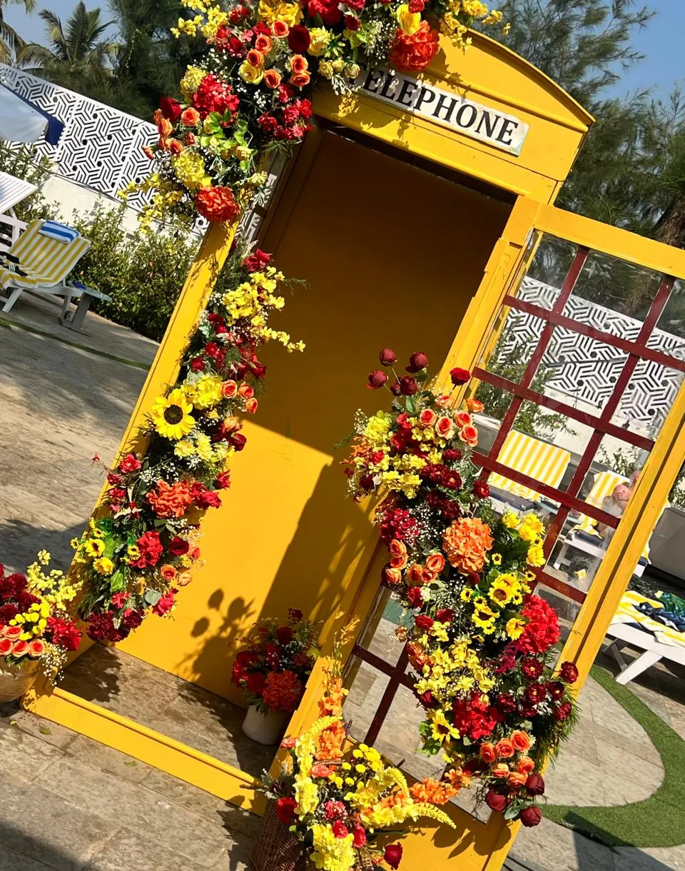 Yellow florist telephone booth photo prop with red roses and sunflowers at a Goa beach event by Imagine Decorators