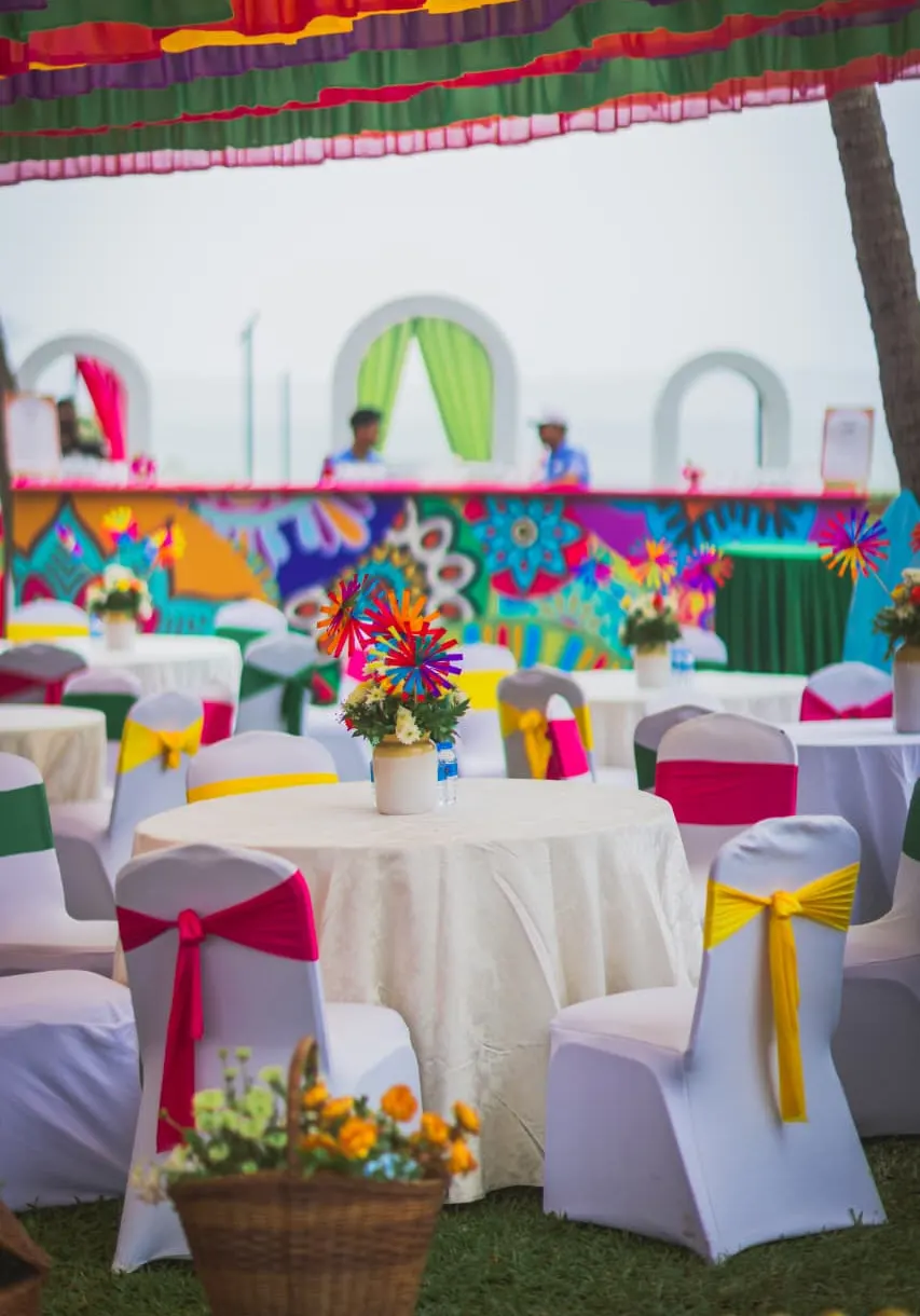 Colourful beach mehendi reception with painted backdrop, vibrant drapes and floral pinwheel centrepieces by Imagine Decorators